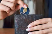 Hand placing a silver Ethereum token into a dark textured wallet