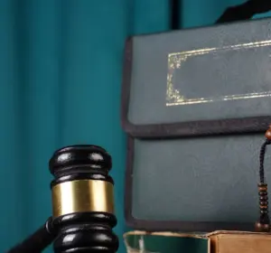 Judge’s gavel beside Islamic book and beads against a teal background.