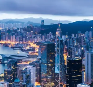 Aerial view of Hong Kong's skyline and harbor at dusk with illuminated skyscrapers and mountains in the background