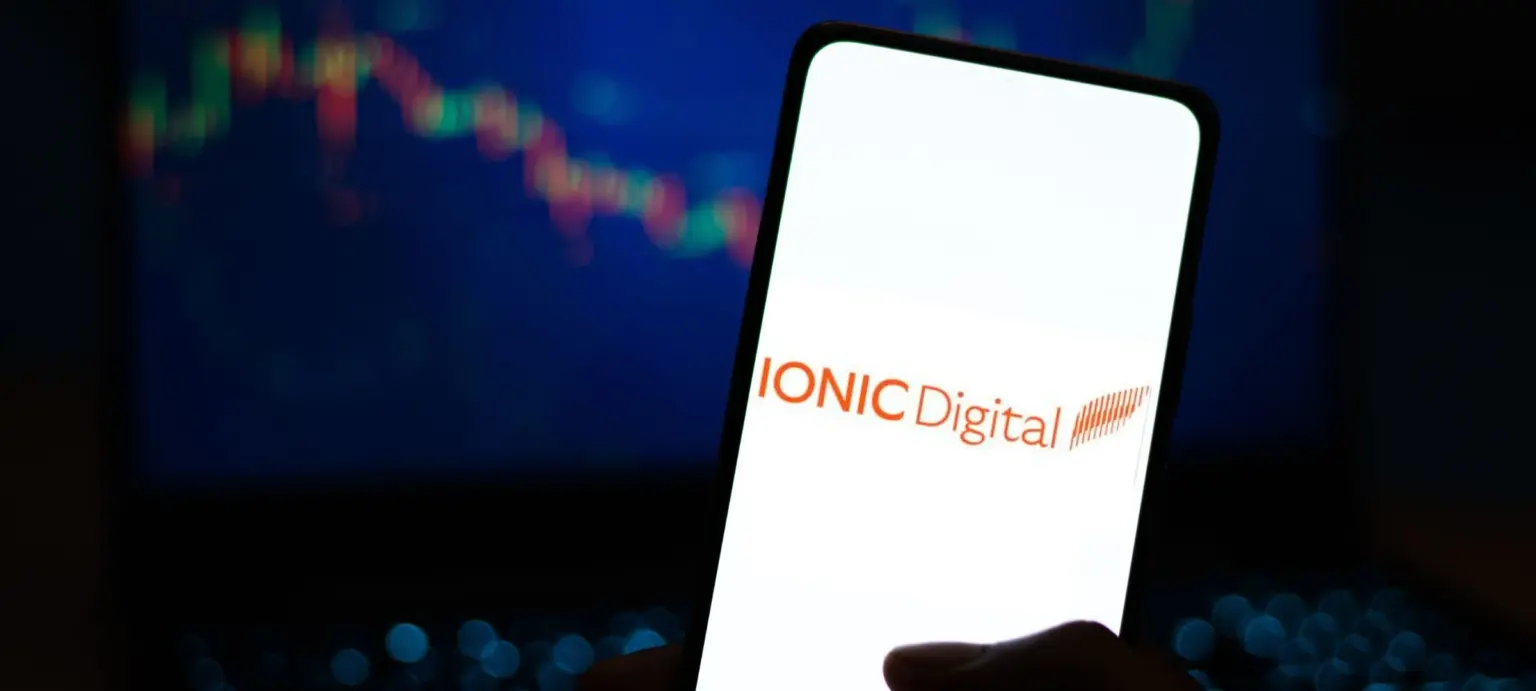 Hand holding a smartphone displaying the Ionic Digital logo with a crypto price chart in the background