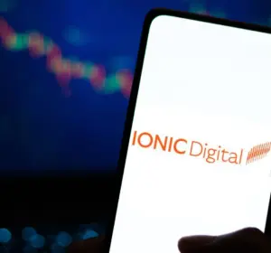 Hand holding a smartphone displaying the Ionic Digital logo with a crypto price chart in the background