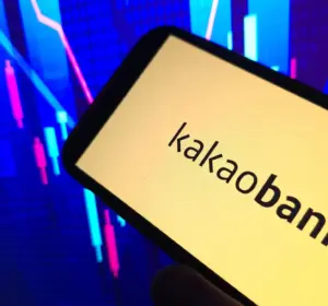 Smartphone displaying the KakaoBank name in front of colorful market chart graphics on a dark background.