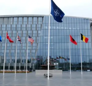 The NATO headquarters building with the NATO flag and multiple member nation flags displayed outside the entrance.