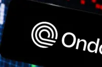 Ondo Finance logo displayed on a smartphone with market charts in the background.