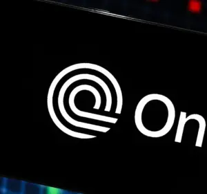 Ondo Finance logo displayed on a smartphone with market charts in the background.
