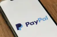 Smartphone displaying the PayPal logo on screen while resting on a wooden surface.