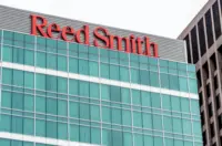 Red Reed Smith sign mounted on the facade of a modern glass office building in a city setting.