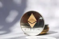 Silver Ethereum token standing beside a small stack of coins on a white surface