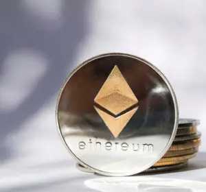 Silver Ethereum token standing beside a small stack of coins on a white surface