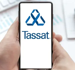 Hands holding a smartphone displaying the Tassat logo above financial charts