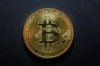 Single gold Bitcoin token resting on a dark textured fabric surface