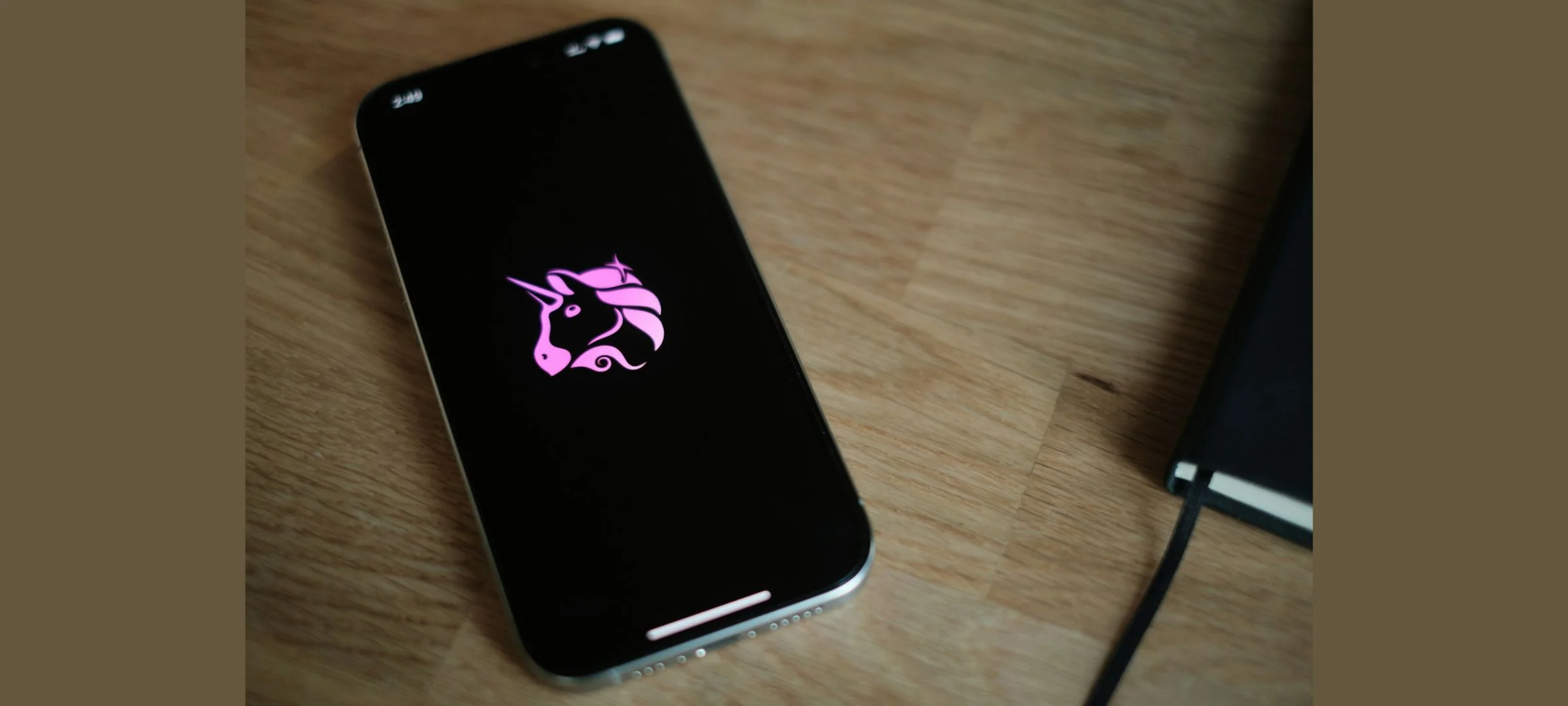 Smartphone displaying the Uniswap unicorn logo on a wooden desk