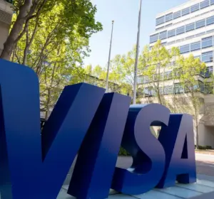 Large Visa sign outside a modern corporate office building on a tree-lined street.