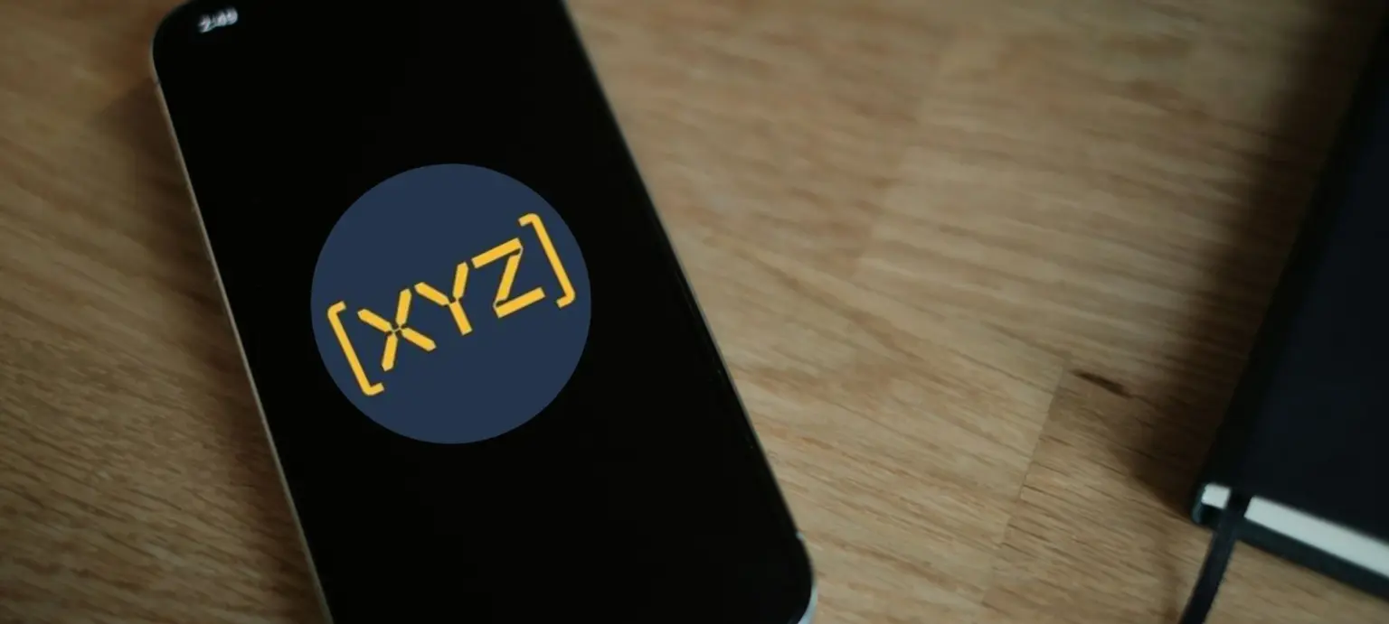 Smartphone lying on a wooden table displaying the [XYZ] app logo