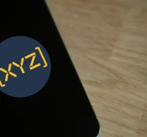 Smartphone lying on a wooden table displaying the [XYZ] app logo