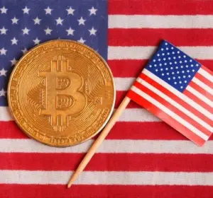 Gold Bitcoin token placed beside a small United States flag on an American flag background