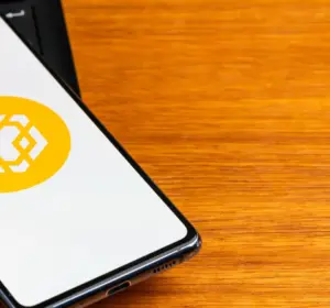 Smartphone displaying the BNB Smart Chain logo while resting on a laptop keyboard beside a wooden desk.