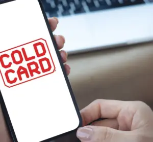 Hands holding a smartphone displaying the Coldcard logo